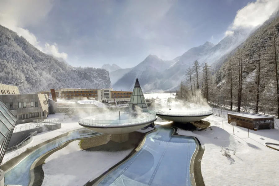 Die dampfenden Außenbecken des Aqua Dome in Längenfeld im Winter, dahinter verschneite Berge